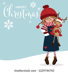 Christmas holiday season background of cute girl in winter costume holding a reindeer doll wears Santa hat with red scarf, gloves and boots on snow floor and blue background with Merry Christmas text.