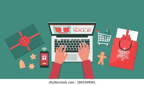 Christmas online shopping or winter holiday sale top view concept, human hand makes order on laptop screen with smartphone gift boxes and shopping bags, flat lay vector illustration