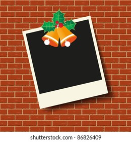 Christmas photo frame with bells and holly berries on the brick wall