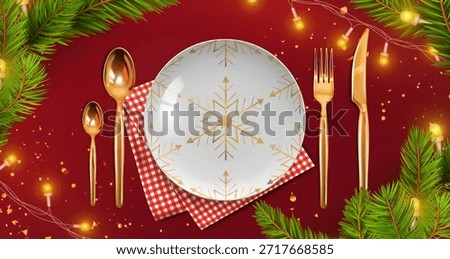 Christmas plate with golden snowflake pattern and cutlery on red bg for holiday table setting. White dish with fork, knife and spoons beside checkered napkin and pine branches with festive lights.