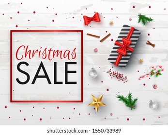 Christmas Sale banner or poster design with top view of gift box, baubles, stars, candy stick, pine leaves and red berries decorated on white wooden texture background.