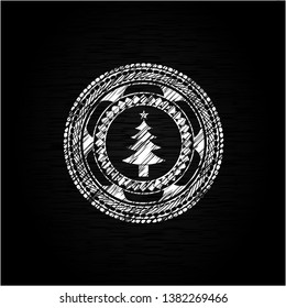 christmas tree icon inside chalkboard emblem written on a blackboard