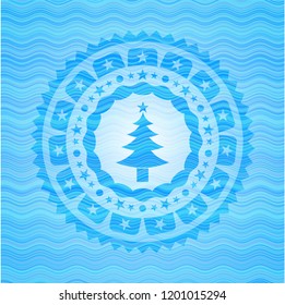  christmas tree icon inside light blue water wave emblem background.