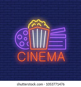 Cinema neon sign. Popcorn box, film reel and clapper board on brick wall. Night bright advertisement. Vector illustration in neon style for online movie and cinema