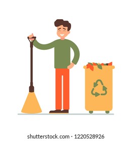 cleaner stands with a broom in his hands. happy young man collected fallen leaves in the garbage bin.  environmental concept for the community work day. 
