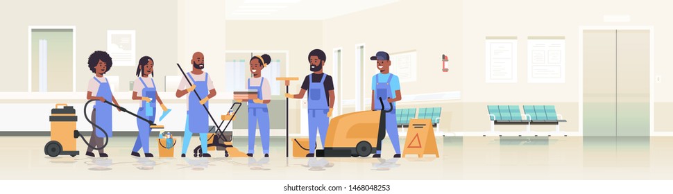 cleaners team in uniform working together cleaning service concept african american janitors using professional equipment clinic reception hospital corridor interior flat full length horizontal