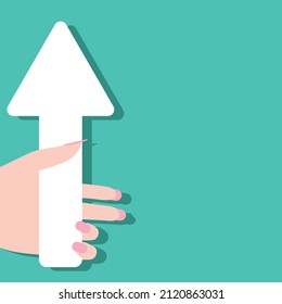 Close-up of a beautiful female hand holding a big white paper arrow up, isolated on a blue-green background, copy space for advertising. Advertising platform, layout, up arrow, female hand