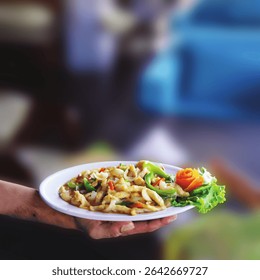 Close-up of a hand holding a white plate of stir-fried chicken with vegetables, garnished with a carved carrot rose and fresh lettuce.