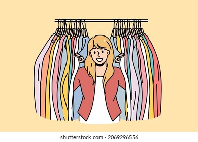 Clothes seller and fashion concept. Young smiling woman cartoon character standing and looking to camera with colorful clothes on hangers both sides vector illustration 