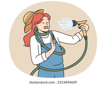 Clumsy woman with garden hose accidentally sprays herself with water while watering backyard lawn during drought. Girl got tangled in garden hose due to failure or lack knowledge of safety precautions