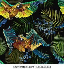 Colorful flying ara parrots, blue flowers and palm leaves seamless pattern. Macaws. Jungle paradise background. Fashionable template for design of clothes, textiles 