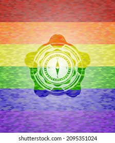 icono de brújula dentro del emblema sobre fondo de mosaico con los colores de la bandera LGBT. 