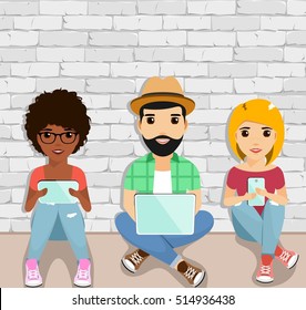 The concept of active users of gadgets. Young people sitting on the floor using gadgets. Happy people