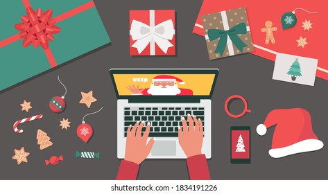 Concept of a human hand using a laptop video call to Santa Claus for Christmas holiday celebration top view table with gifts, cookies, candy, Santa hat, and postcard, flat lay vector illustration