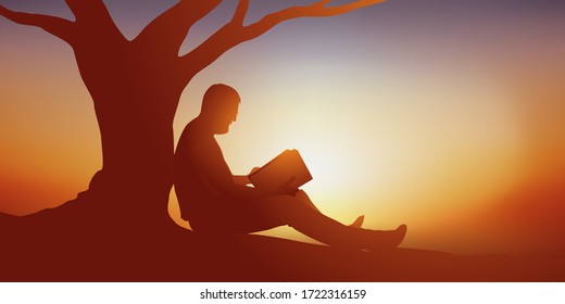 Concept of a moment of relaxation with a man who takes advantage of a moment of solitude and tranquility to read a book at the foot of a tree.