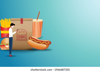 Concept of online fast food delivery service, young man standing in front of a big hamburger bag to order fast food (sparkling water, hot dog, hamburger and french fries) in green color background.