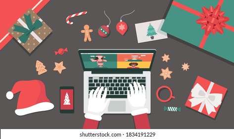 Concept of Santa Claus hand using a laptop video call to people for Christmas holiday celebration top view table with gifts, cookies, candy, Santa hat, and postcard, flat lay vector illustration