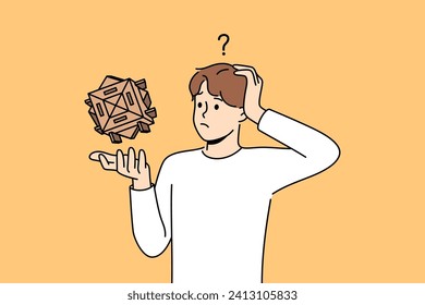 Confused man with wooden puzzle scratches head, wondering how to solve difficult problem. Thoughtful guy with puzzle needs help to find solution due to lack of necessary qualifications