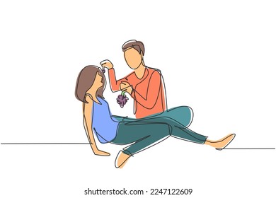 Continuous one line drawing romantic couple having picnic in summer park. Relaxing together sitting on the ground and men feeding grapes to women. Single line draw design vector graphic illustration