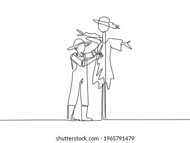 Continuous one line drawing a young male farmer in a straw hat is putting up a scarecrow to keep out pests of birds. Farming minimalist concept. Single line draw design vector graphic illustration.
