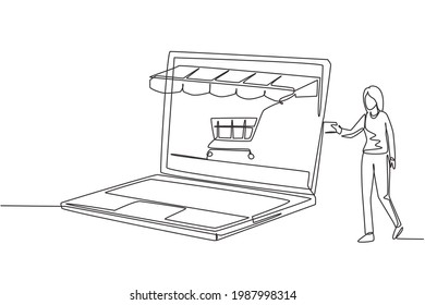 Continuous one line drawing young woman inserting credit card into large canopy laptop screen with shopping cart. E-shop, digital payment concept. Single line draw design vector graphic illustration