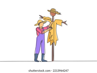 Continuous one line drawing a young male farmer in a straw hat is putting up a scarecrow to keep out pests of birds. Farming minimalist concept. Single line draw design vector graphic illustration.