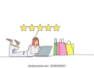 Continuous one line drawing young Arabian man on stomach while typing on laptop. Next to the laptop is a shopping bag. Give the best review with pleasure. Single line draw design vector illustration