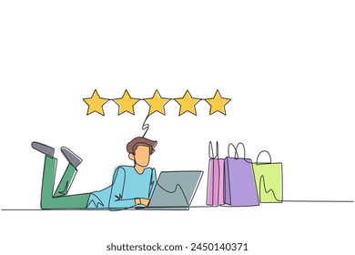 Continuous one line drawing young smiling man on stomach while typing on laptop. Next to the laptop is a shopping bag. Give the best review with pleasure. Single line draw design vector illustration