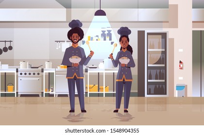 cooks couple professional chefs holding plates with porridge african american workers in uniform tasting dishes cooking food concept modern restaurant kitchen interior flat full length horizontal