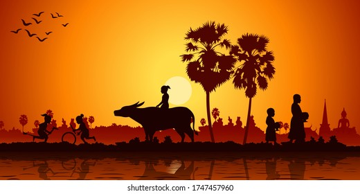 Country life of Asia children play banana horse ride buffalo while monk receivex food.  Sunrise time silhouette style