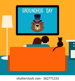 Couple and cat watching television sitting on couch in  room. Groundhog day theme.  Groundhog day card. Couple on couch and tv. Room interior. Cat on couch. Couple at home. Interior with couch and tv.