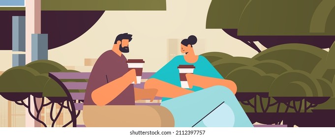 couple drinking coffee during meeting in urban park man woman sitting on wooden bench cityscape background