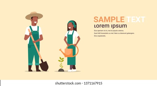 couple farmers planting tree man with shovel woman holding watering can african american gardeners working in garden agricultural gardening concept full length copy space horizontal