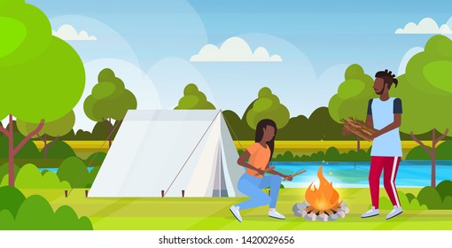 couple hikers making fire man woman holding firewood for bonfire hiking concept african american travelers on hike tent camping nature landscape background horizontal full length flat