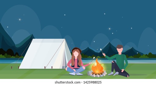 couple hikers roasting marshmallow candies on campfire hiking camping concept man women travelers on hike night mountains landscape nature background horizontal full length flat
