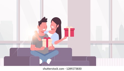 couple holding present wrapped gift boxes man woman embracing sitting couch celebrating holiday concept happy lovers modern living room interior horizontal