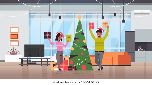 couple holding wrapped gift present boxes merry christmas happy new year holiday celebration concept man woman wearing santa hats modern living room interior flat full length horizontal vector