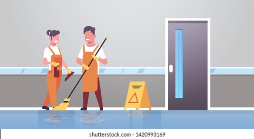 couple janitors man woman in uniform cleaning service concept cleaners holding mop spray plastic bottle working together modern clinic corridor interior full length flat