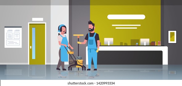 Couple Janitors Man Woman In Uniform Working Together Cleaning Service Concept Cleaners Pushing Trolley Cart With Tools Modern Hospital Reception Interior Full Length Flat Horizontal