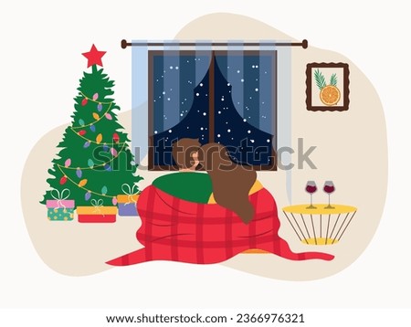 A couple in love in a blanket, looking out the window. The window next to the Christmas tree and gifts. A couple sits in an embrace and looks out the window, next to a coffee table with glasses of win
