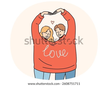 Couple in love wearing same sweater together makes heart shape from hands, showing sympathy and passion. Guy and girl with inscription love on clothes congratulate you on valentine day