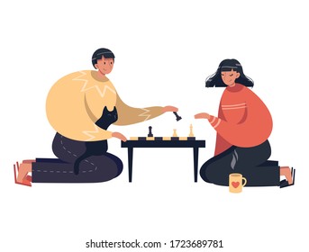 Couple plays chess at home sitting on the floor. Cozy home furnishings, hot tea, cat, board games with family. Games for two, educational games, chess. Joint pastime during quarantine, self islation.