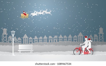 Couple riding a red bike in white Urban Countryside and Santa Claus on the sky  with snow in winter season, Paper art and Illustration