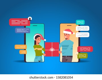 couple in santa hats using chatting app social network chat bubble communication concept man woman in smartphone screens holding gift box online mobile application portrait vector illustration