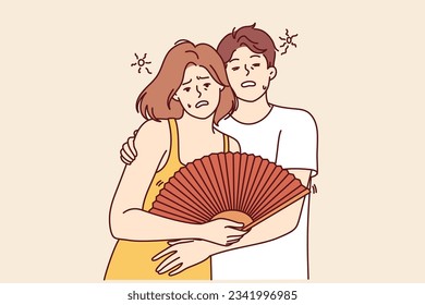 Couple suffers from sunstroke during summer heat and hugs feeling exhausted due to climate change. Man and woman with fan need refreshments and cool room after sunstroke caused by global warming.