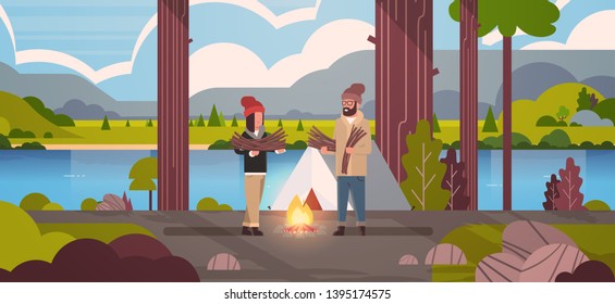 couple tourists hikers holding firewood man woman organizing fire near camp tent hiking camping concept landscape nature river mountains background flat horizontal full length