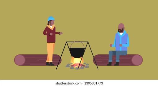 couple of tourists hikers man woman cooking meals in bowler boiling pot at campfire hiking camping concept african american travelers on hike horizontal full length flat
