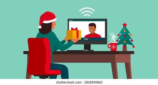 Couple video caling at Christmas: the woman is giving a gift to her partner and he is smiling, social distancing concept