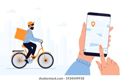 COVID-19. Quarantine. Coronavirus epidemic. Delivery man in a protective mask delivers parcel by bike. Track shipments using the mobile application. Hand is holding smartphone