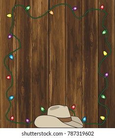A cowboy hat is resting on the ground in front of a barn wall decorated with Christmas lights